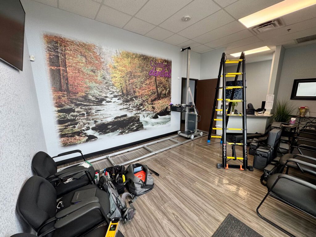 ArtWall Pro mural installation at Comfort Dental, featuring a large wall print of a forest stream with autumn trees in the patient waiting area.